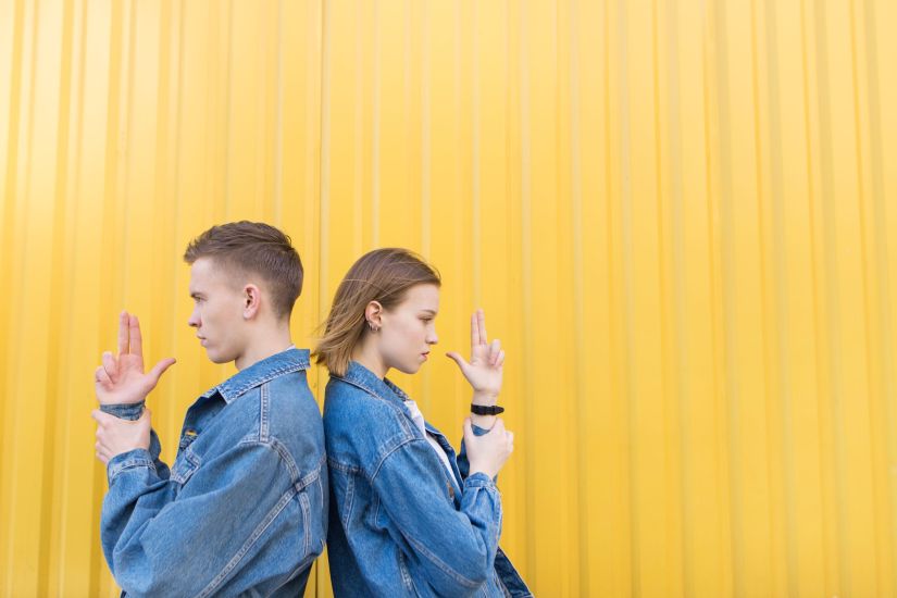 Man and girl against a bright yellow wall. Stylish young couple standing back to back on holding hands in the form of arms